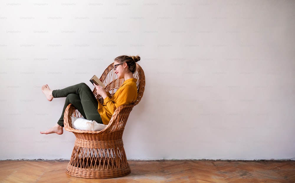 Una joven estudiante feliz sentada en una silla de mimbre, leyendo. Espacio de copia.