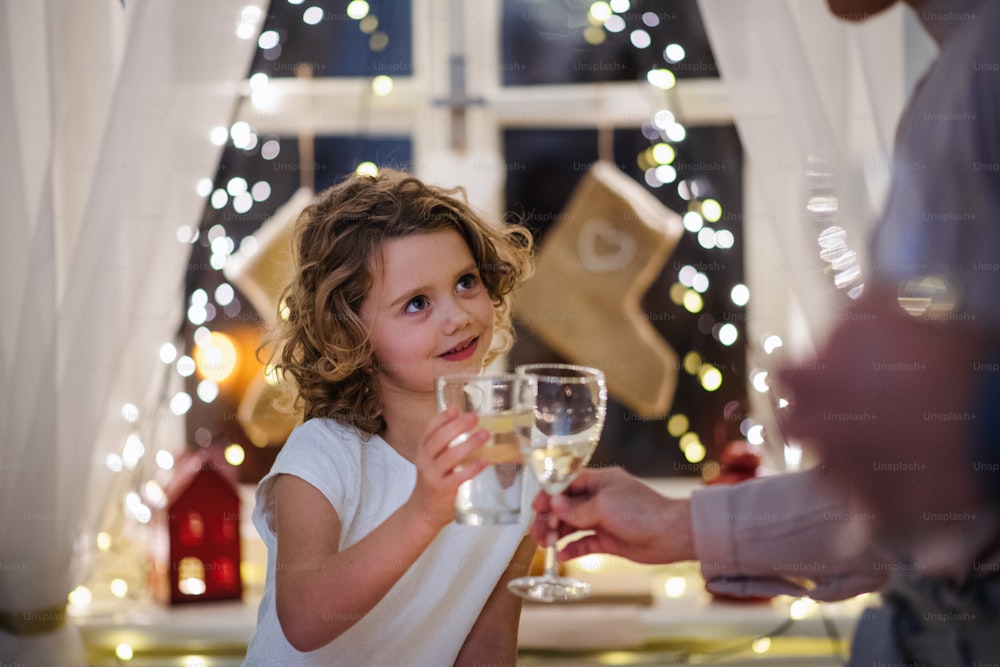 Glückliches kleines Mädchen mit Familie, das drinnen sitzt und Weihnachten zusammen feiert und mit den Gläsern klirrt.
