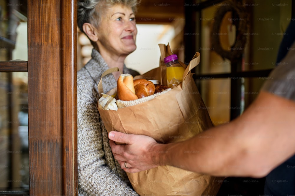Coursier méconnaissable livrant des courses dans un sac en papier à une femme âgée.