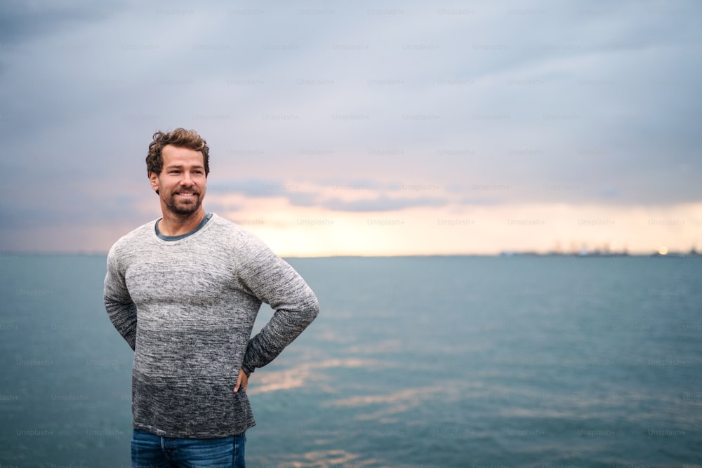 Portrait of mature man standing outdoors on beach at dusk. Copy space.