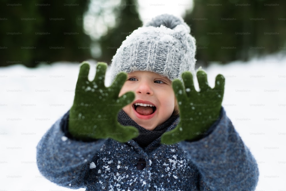 Front view of cheerful small child standing in snow, holiday in winter nature.