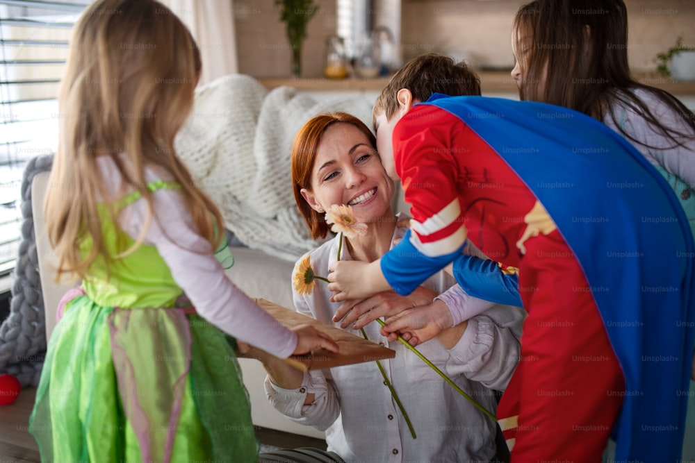 A mother of little children in costumes getting present from them at home.