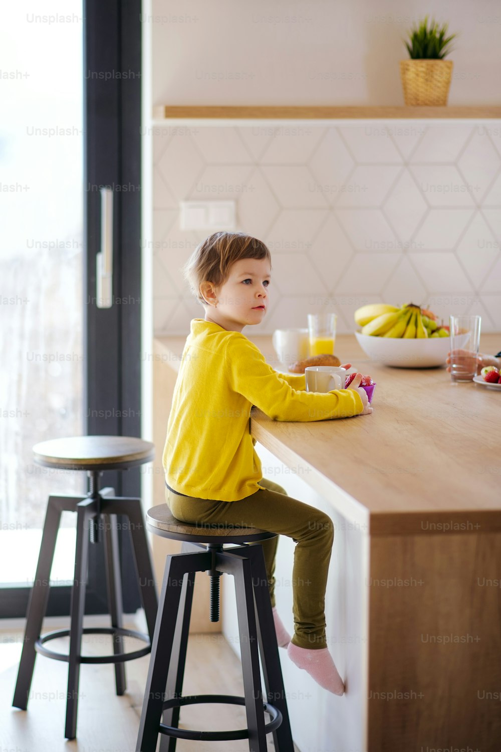 Una bambina seduta su uno sgabello in cucina a casa, che mangia frutta.
