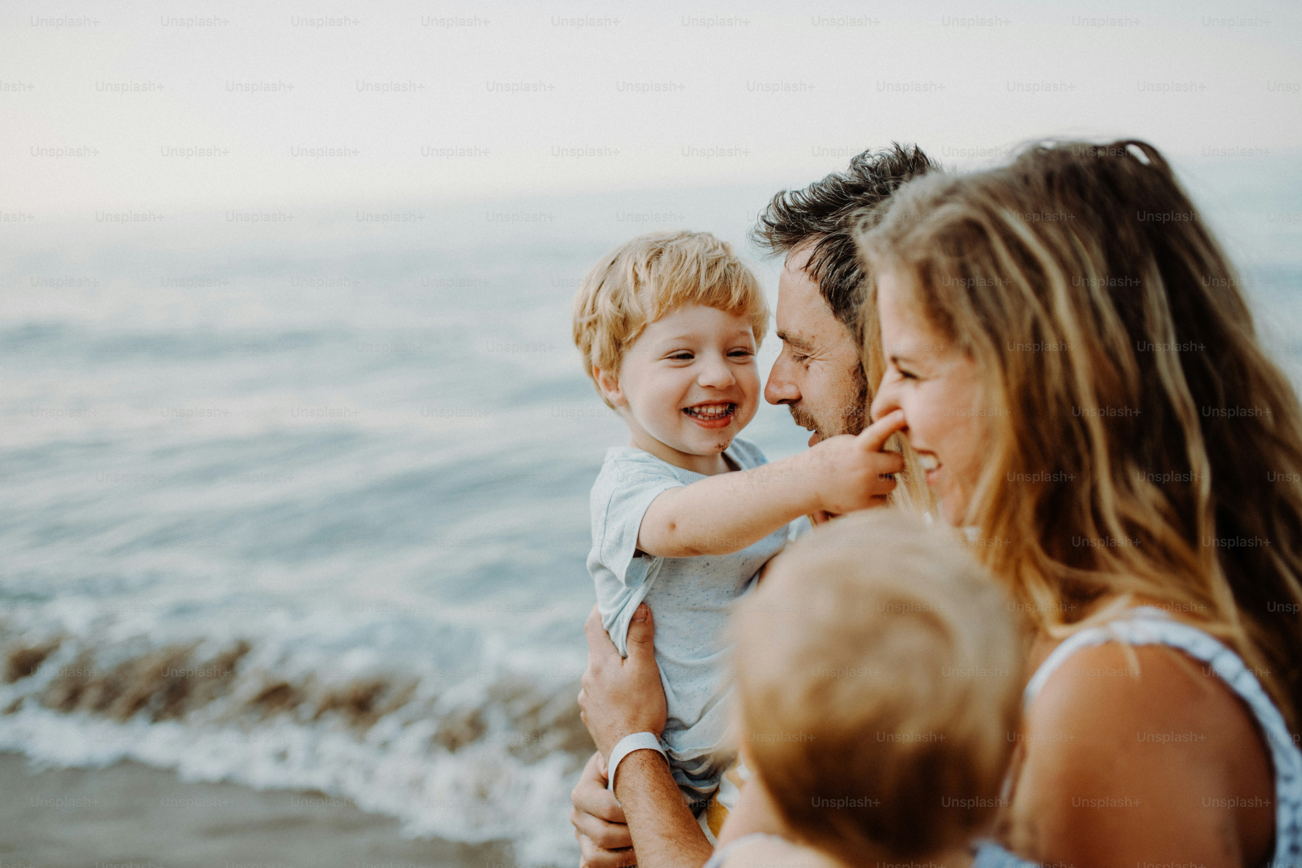 A young family with two toddler children standing on beach on summer holiday, laughing