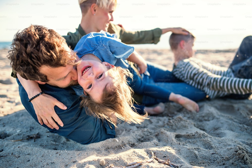 Portrait of young family with two small children lying down outdoors on beach, having fun.