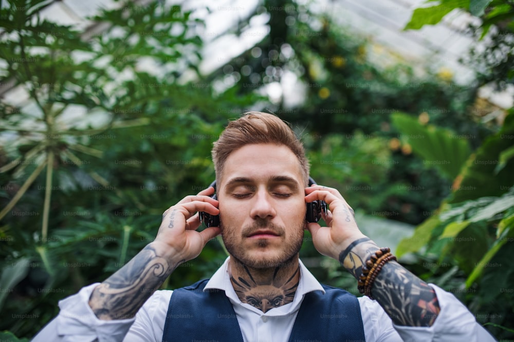 Hombre joven con auriculares de pie en invernadero en jardín botánico. Concepto de negocio verde.