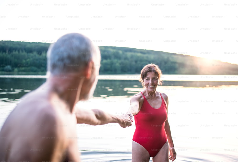 수영하기 전에 야외 호수에 서 있는 수영복을 입은 쾌활한 노부부.