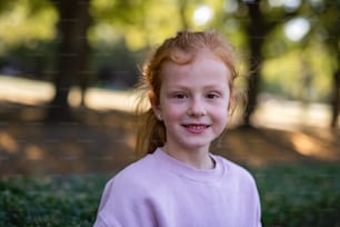 주근깨와 빨간 머리를 가진 행복한 어린 소녀가 카메라를 보고 공원에서 야외에서 웃고 있다.