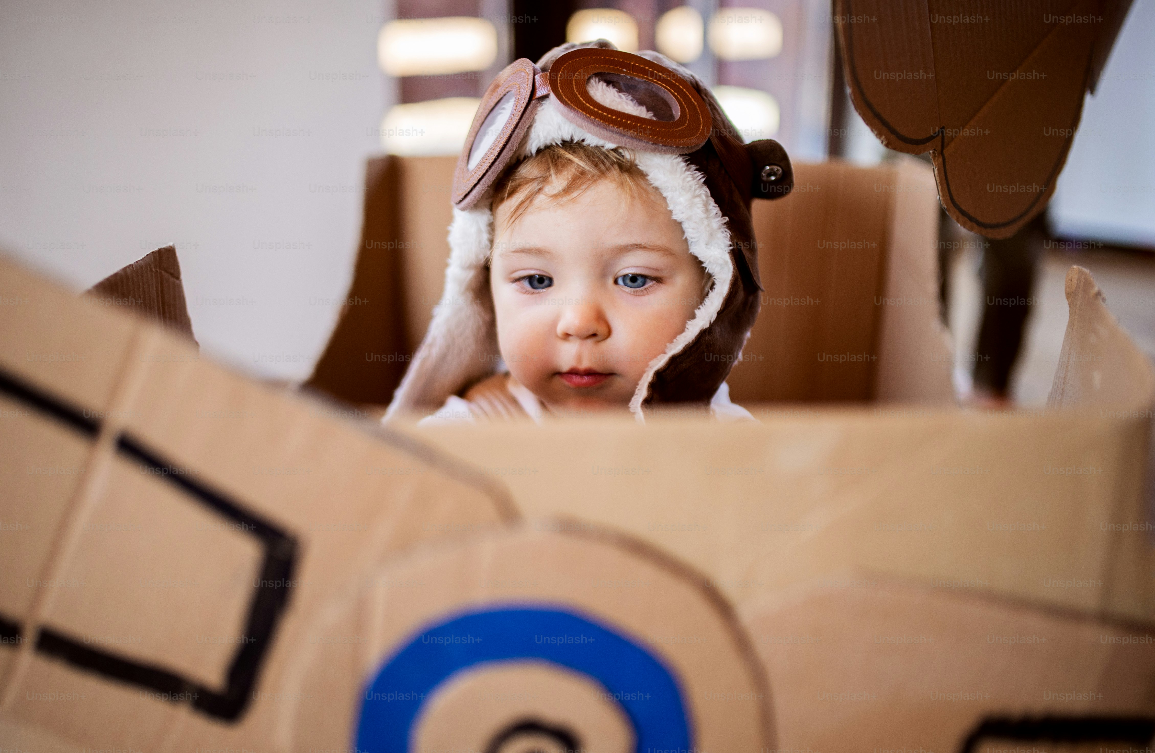 A toddler girl with carton plane and clouds playing indoors at home, flying concept.