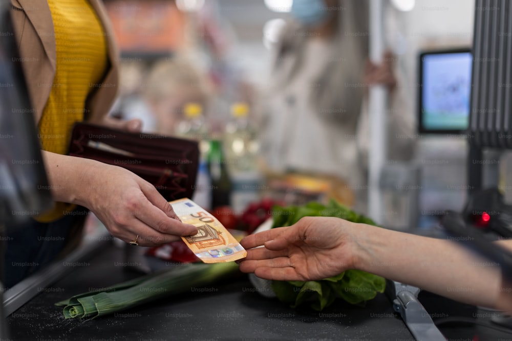 Un gros plan d’une femme donnant de l’argent à la caisse d’un supermarché
