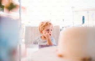 夏休みに屋外のレストランに座り、鼻をほじる小さな男の子。