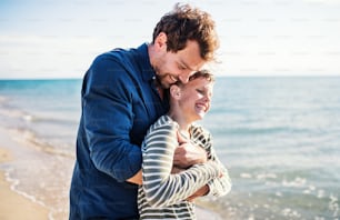 Father with small son hugging on a walk outdoors on beach, having fun.