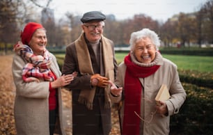 A group of happy senior friends on walk outdoors in town park in autumn, looking at camera.
