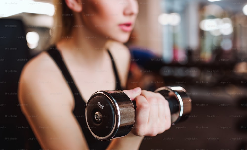 A midsection of young girl or woman with dumbbells, doing workout in a gym.