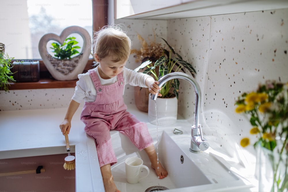 Une petite fille assise sur le comptoir de la cuisine et laver la tasse dans l'évier de la cuisine.