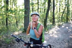 Ein Porträt einer aktiven älteren Bikerin, die draußen im Wald einen Helm aufsetzt.