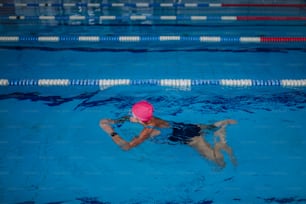 A high angle view of active senior woman swimming in indoors swimming pool.