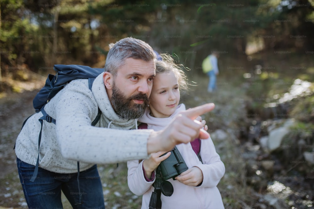 Un padre con una hija pequeña con binoculares en un paseo por la naturaleza primaveral juntos.