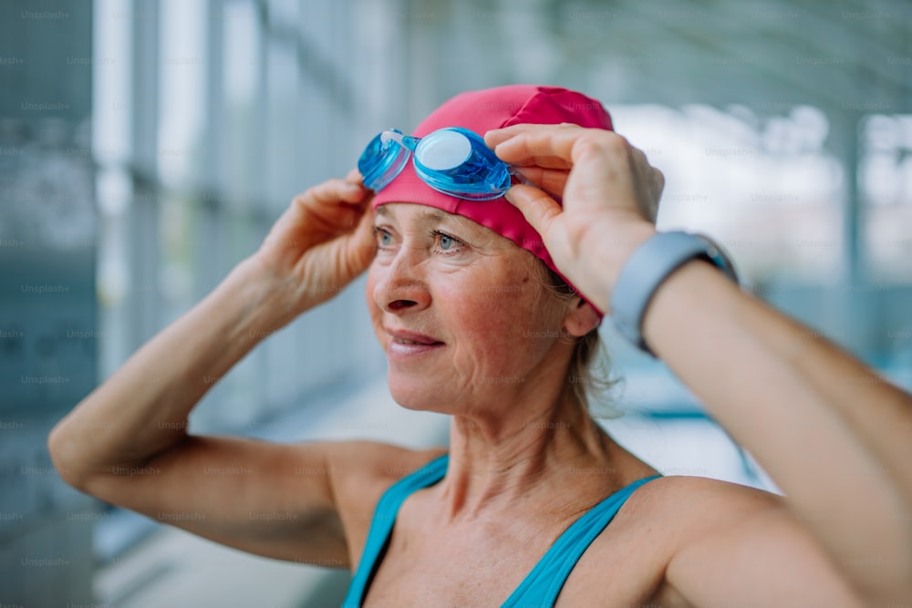 A close-up of senior woman putting on goggles before swim in indoors swimming pool.