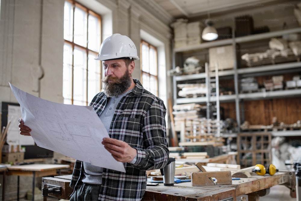 Un carpintero maduro mirando planos planos en un taller de carpintería. Concepto de pequeña empresa.