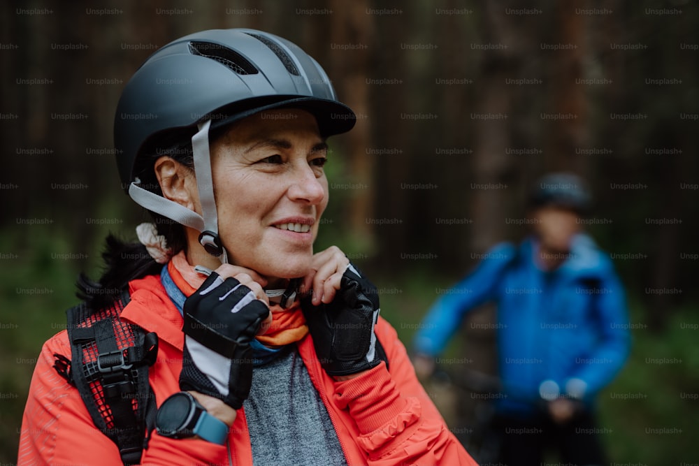 Una motociclista de alto nivel que se pone un casco de ciclismo al aire libre en el bosque en un día de otoño.