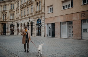 Un elegante uomo anziano con caffè da asporto che porta a spasso il suo cane all'aperto in città in inverno.
