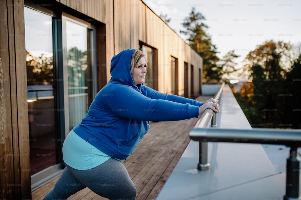 Una mujer adulta mediana de talla grande que se estira después de hacer ejercicio entrenando al aire libre en la terraza del gimnasio