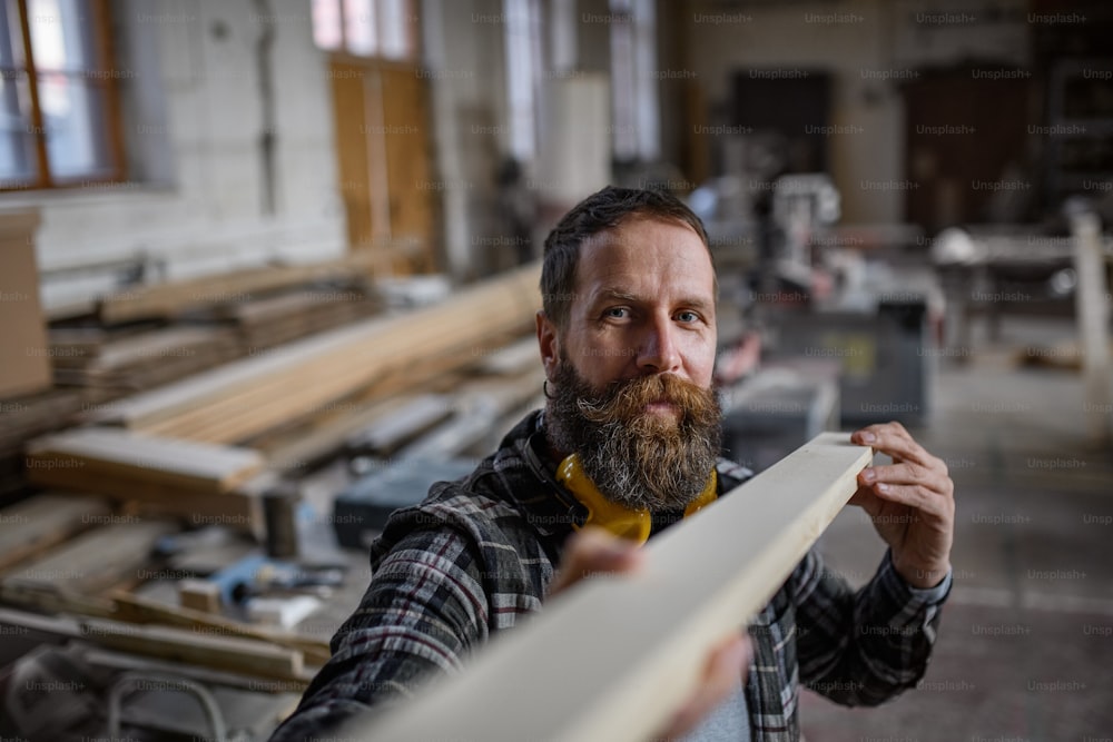 Un carpintero maduro que lleva tablas de madera al interior de un taller de carpintería. Concepto de pequeña empresa.