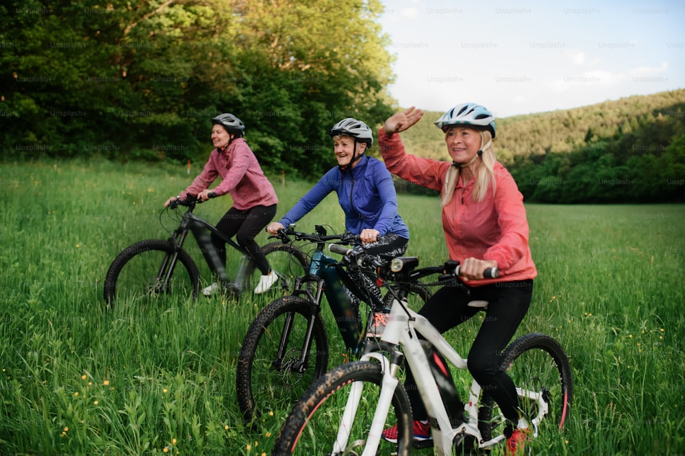 Happy active senior women friends cycling together outdoors in nature in meadow.Happy active senior women friends cycling together outdoors in nature in meadow.