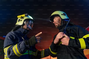 Un irefighter de vista de ángulo bajo recibiendo instrucciones del jefe con un camión de bomberos en el fondo por la noche