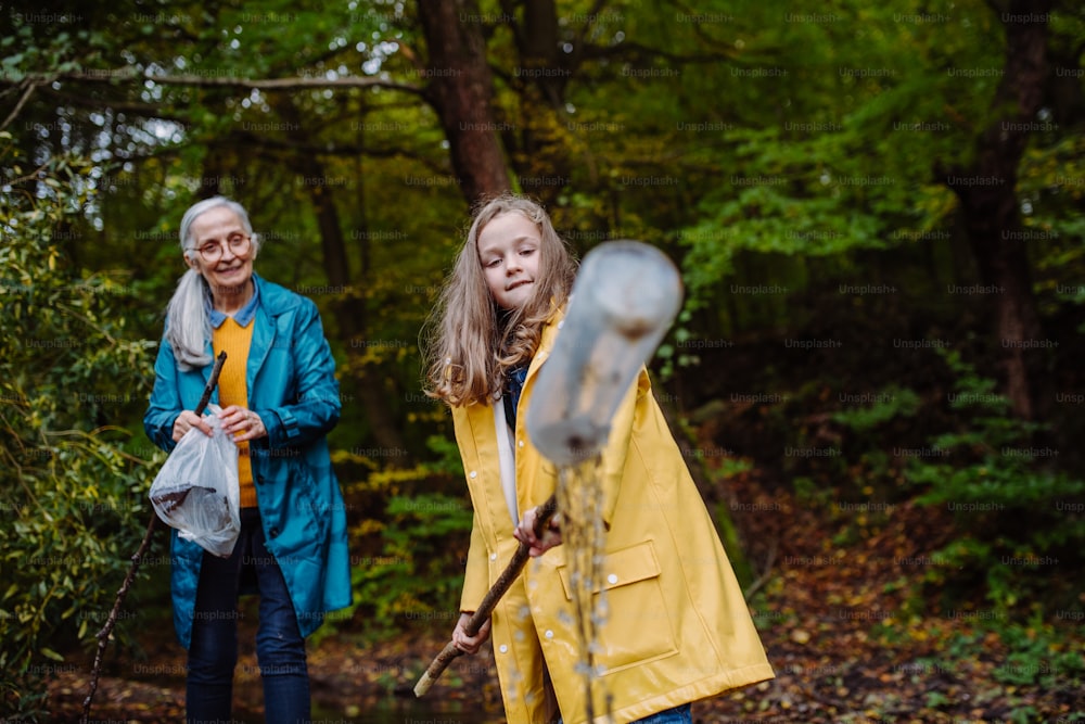 A small girl with grandmother showing plastic waste what they found outoors in forest.