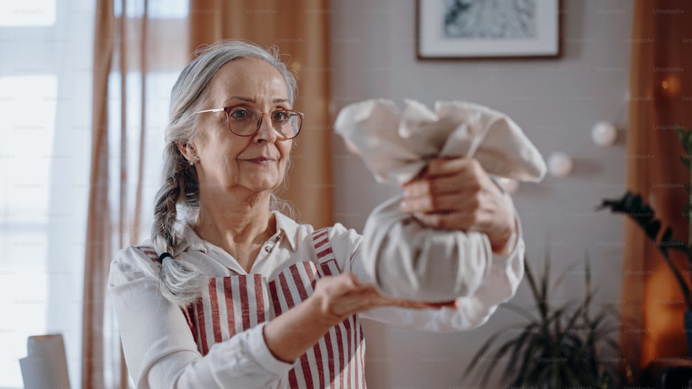 A senior woman holding Christmas present wrapped in eco materials indoors at home.