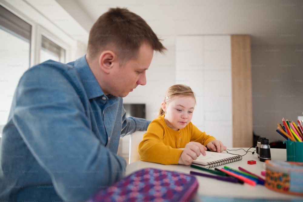 Ein Vater mit seiner kleinen Tochter mit Down-Syndrom lernt zu Hause.