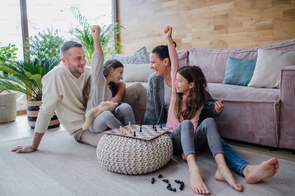 母親と父親が床に座り、家で一緒にチェスをしている幸せな姉妹