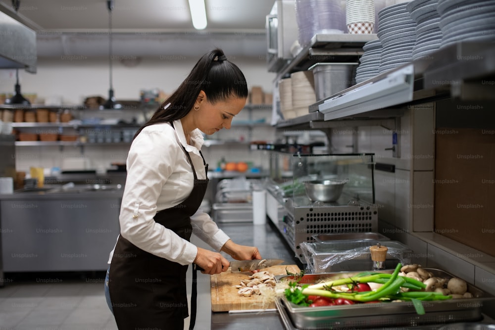 A professional female chef cutting vegetables indoors in restaurant kitchen.