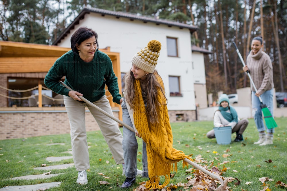 A happy little girls with grandmother and mother cleaning up garden from leaves in autumn