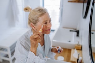 Une belle femme âgée en peignoir, hydratant la peau à la pipette avec du sérum appréciant la procédure de traitement.