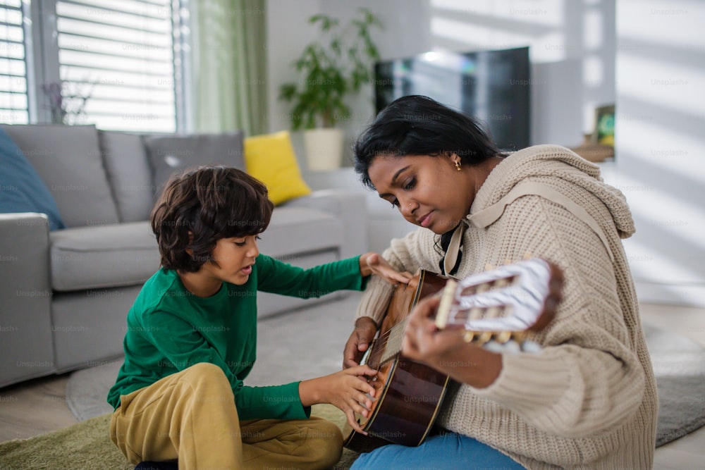 집에서 어머니와 함께 기타 연주를 배우는 작은 다인종 소년.