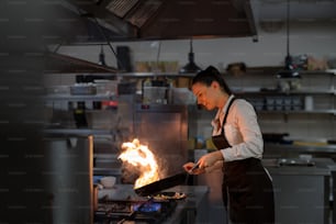 Uno chef professionista che prepara il pasto, fiammeggiando all'interno nella cucina del ristorante.