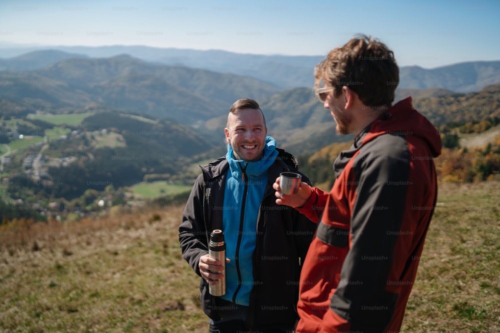 山の頂上に立ってお茶を飲む2人のパラグライダーの男性。