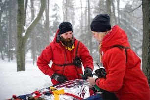 山岳救助隊の救急隊員が、冬季の森林や負傷者を担架に乗せて屋外で活動します。