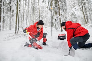 Mountain rescue service on operation outdoors in winter in forest, digging snow with shovels. Avalanche concept.