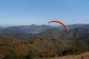 A paraglider flying in the blue sky with mountain in background.