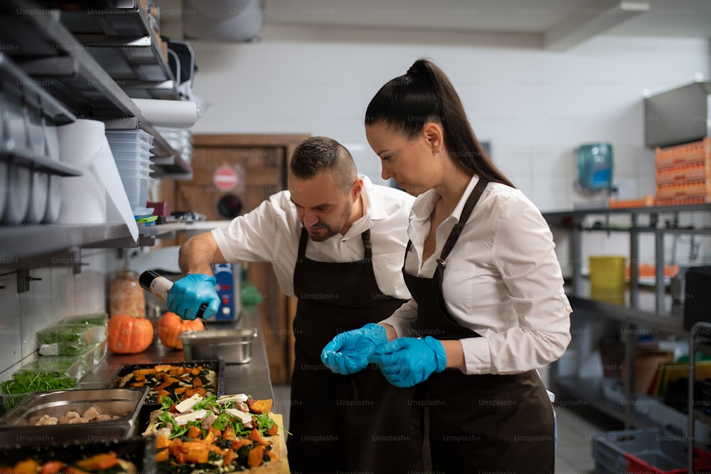 Un chef et un cuisinier travaillant sur leurs plats à l’intérieur dans la cuisine d’un restaurant.