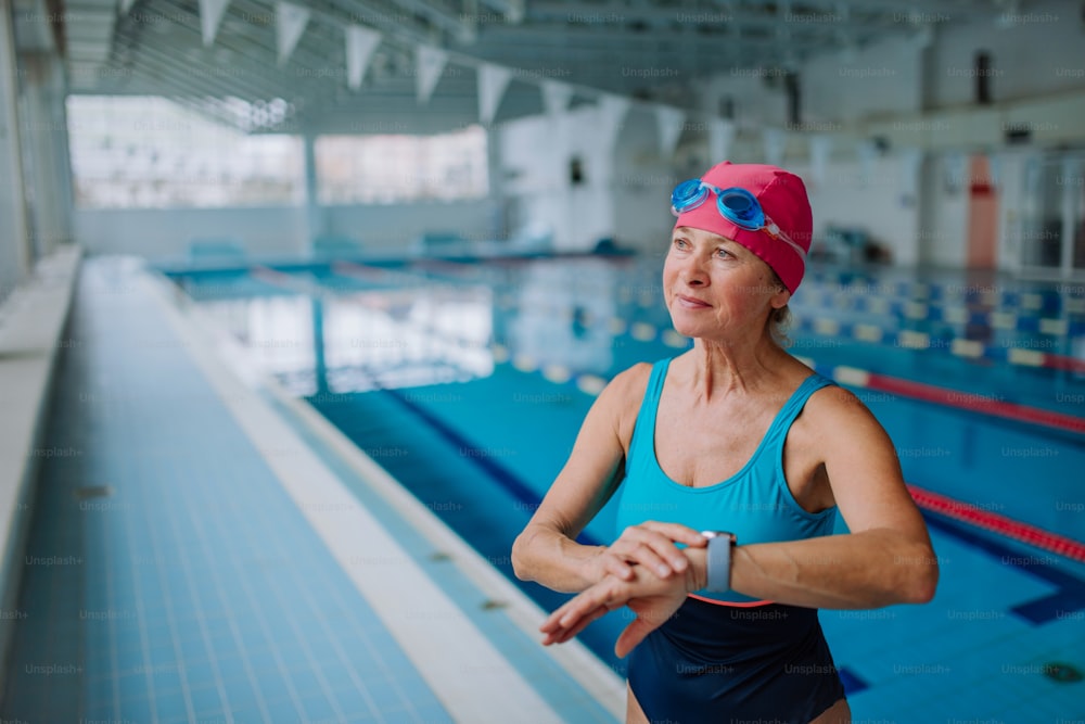 A senior woman setting smartwatch before swim in indoors swimming pool.