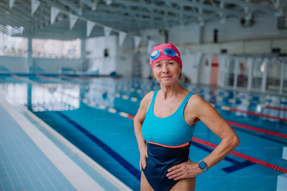 An active senior woman looking at camera and smiling after swim in indoors swimming pool.