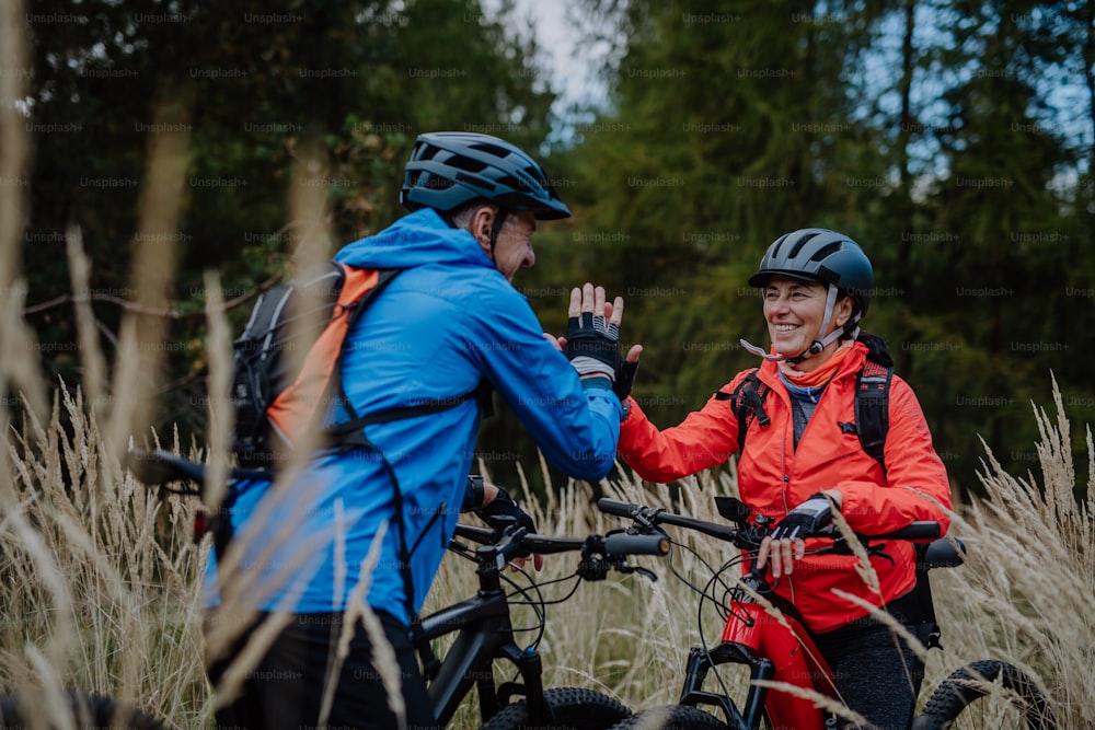 A senior couple bikers high fiving outdoors in forest in autumn day.