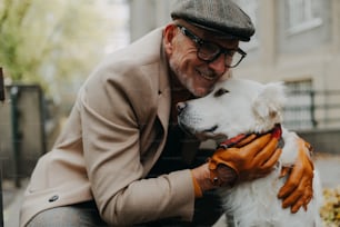 A happy senior man sitting on bench and embracing his dog outdoors in park in city.