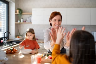 A happy mother high fiving with little daughter when having breakfast in kitchen at home.