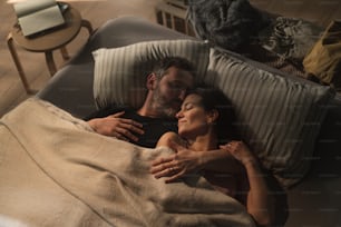 An overhead view of mid-adult couple lying in bed at night and hugging and looking at each other.